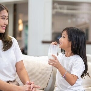 An Asian mom smiling at her daughter holding a glass of milk for the benefits of milk.