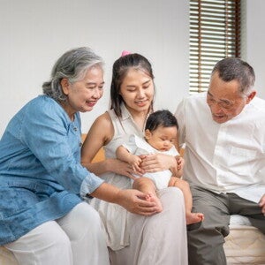 Asian grandparents look lovingly at their grandchild who is held by their mother on her lap.
