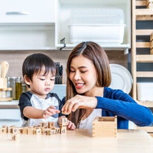 A young Asian mother and her little son stack wooden blocks to boost brain development.