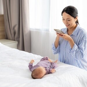 Asian mom getting a clear baby picture of her little one lying on a white bed overhead.