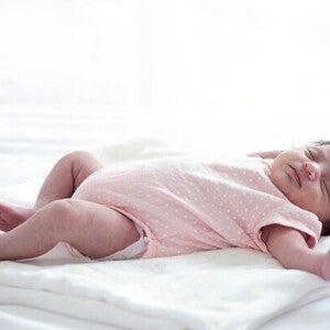 An Asian newborn girl is startled while asleep, triggering the Moro reflex, jerking arms outwards. 