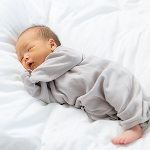 Asian newborn grunting while sleeping on white sheets.
