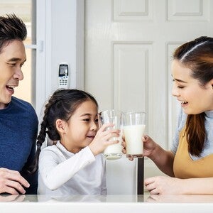 Asian dad looking at his school-aged daughter and wife clinking glasses full of fresh milk and growing-up milk.