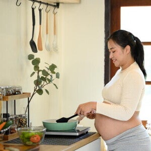 An pregnant Asian woman cooking food for pregnant women at home in her kitchen.