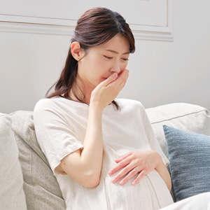 Photo of a pregnant Asian woman with her hand to her mouth, experiencing acid reflux in pregnancy.