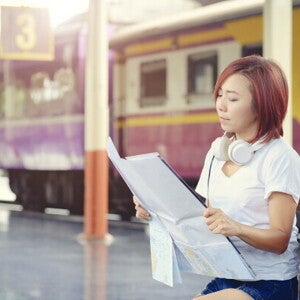 Asian woman reading a map in front of a train. 