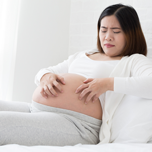 Asian pregnant women scratching her belly as a symptom of a pregnancy rash.