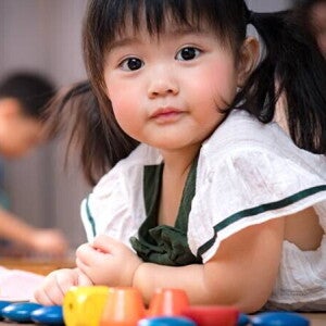 Asian 2-year-baby girl lies on her stomach on the floor while playing with her toys.