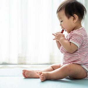 Asian baby sitting on a mat about to put a choking hazard in his mouth Asian baby sitting on a mat about to put a choking hazard in his mouth