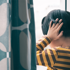 Asian child with special needs covers his ears as he faces the window