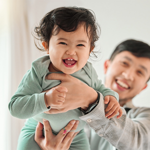 Asian dad lifts his laughing baby with both hands high in the air 