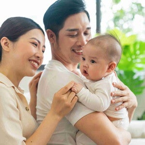 Asian dad with his wife behind him carries their healthy baby in his arms. Asian dad with his wife behind him carries their healthy baby in his arms.