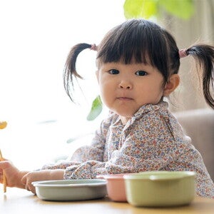 Asian female toddler prepares to eat as she holds her fork with food Asian female toddler prepares to eat as she holds her fork with food