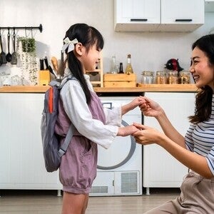 Asian mom holding little girl’s hand in the kitchen after giving her baon bag with milk products for school