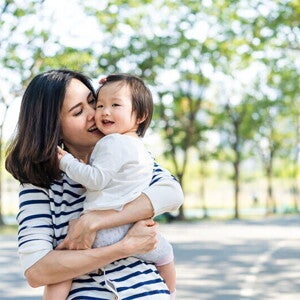 Asian mom kisses her toddler while carrying her in her arms during a walk in a park