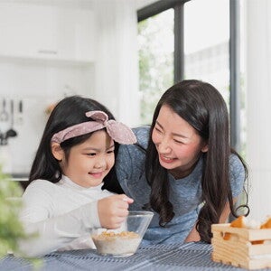 Asian mother watching her child eating cereal from a bowl Asian mother watching her child eating cereal from a bowl