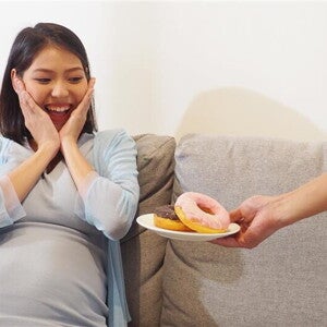 Asian pregnant woman reacts with a big smile as she's offered donuts on a plate. Asian pregnant woman reacts with a big smile as she's offered donuts on a plate.