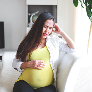 Asian pregnant woman winces in pain due to heartburn
