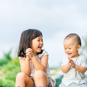 Asian preschool-age girl and her baby brother laugh as they play a game outdoors