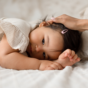 Asian toddler with respiratory tract infection lies face down as her parent strokes her head