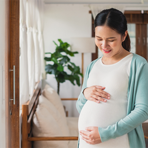 Asian woman at 27 weeks pregnant holds her baby bump