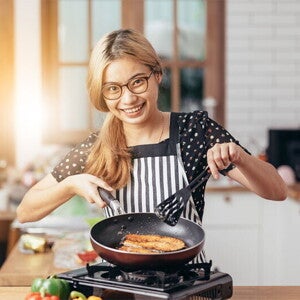 Asian woman frying fish in a pan in her kitchen Asian woman frying fish in a pan in her kitchen