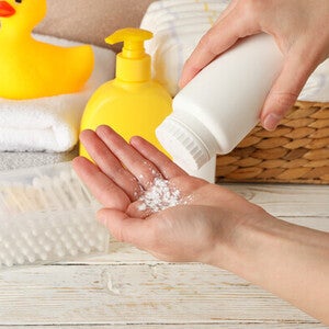 Close-up pic of one hand pouring baby powder onto the other hand, with towels and a yellow rubber duck in the background.
