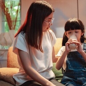 Asian mom watching her little girl drinking milk before bed, wondering does milk help you sleep?