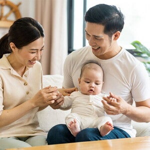 Filipino mom smiles at her newborn who's being held by her husband on his lap. Filipino mom smiles at her newborn who's being held by her husband on his lap.