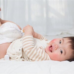Hands holding a smiling Asian baby’s legs and removing the diaper to check baby poop color. Hands holding a smiling Asian baby’s legs and removing the diaper to check baby poop color.