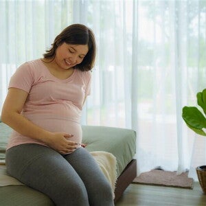 Happy pregnant Asian woman touches her pregnant belly while sitting on the bed. Happy pregnant Asian woman touches her pregnant belly while sitting on the bed.
