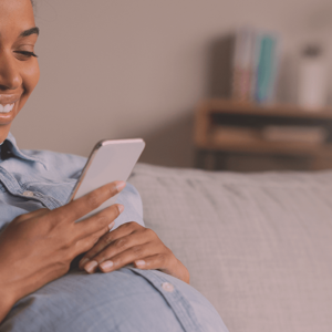 Pregnant woman sitting on a couch, looking at her smarphone and smiling. Pregnant woman sitting on a couch, looking at her smarphone and smiling.