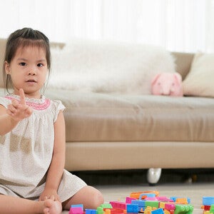  A little Asian girl sitting on the floor in living room, counting with her fingers, using math for kids.