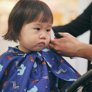 Little Asian girl getting a toddler haircut at a kid’s salon.