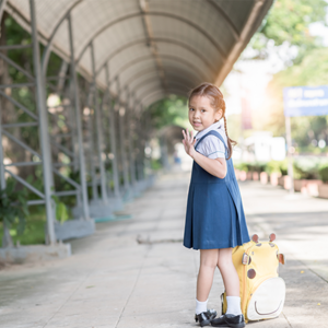 Little Asian girl going back to school with her backpack, waving