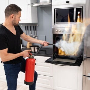 A young man using a fire extinguisher to put out a fire in an oven after learning fire safety tips. 