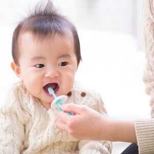 Cropped pic of mom’s hand brushing her infant’s teeth with baby toothpaste.