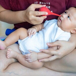 Cropped photo of a mom using a bulb syringe nasal aspirator to suck out snot from her baby’s nose.