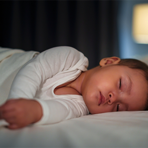 Newborn baby in a white onesie asleep in bed in the evening. Newborn baby in a white onesie asleep in bed in the evening.