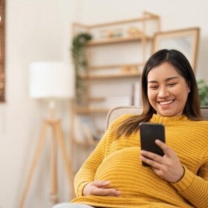Pregnant Asian woman using her phone to message her ob-gyne for her birth plan.