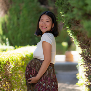 Smiling pregnant Asian woman wearing a cotton dress outdoors and showing off her baby bump.