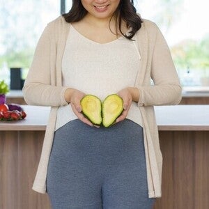 Pregnant Asian woman holding a sliced avocado—one of the best fruits for pregnant women