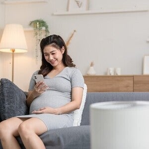 Pregnant Asian woman on a sofa looking at her pregnancy app on her phone at home