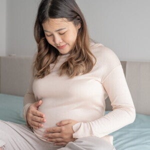Pregnant Asian young woman who is 32 weeks pregnant stares at her baby bump 