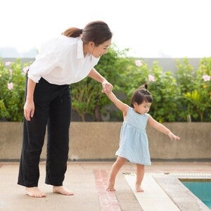 Asian mom holding preschooler daughter’s hand by the edge of the pool, teaching her water safety rules. 