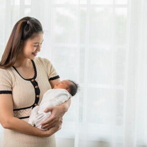 A new mom holding her newborn baby while standing at home, happy with her self-care plan.