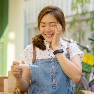Asian woman in denim jumping smiling at pregnancy test results.