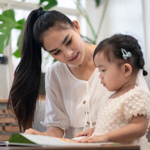 A young Asian mother and her daughter reading a Filipino children’s book together. 