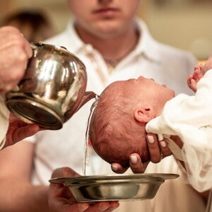Catholic priest pours water over a baby's head for a christening or baptism ceremony.