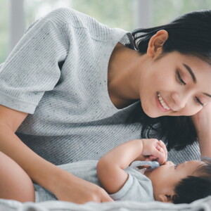Young Filipino mom smiles down at her baby as she lies down beside them.